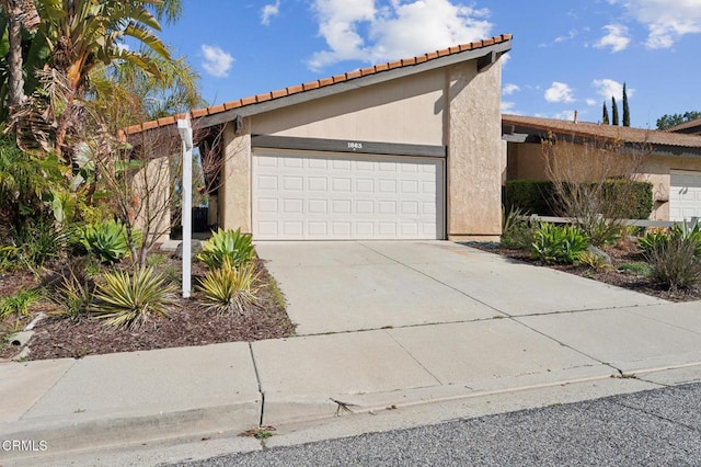 view of front of home featuring stucco siding, an attached garage, a tile roof, and driveway
