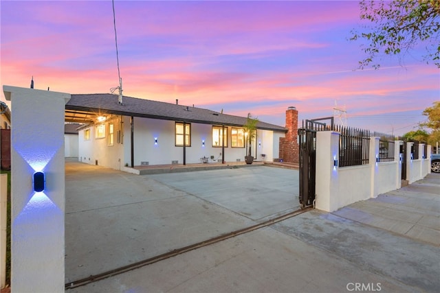 back of house at dusk featuring driveway, a fenced front yard, a gate, and stucco siding