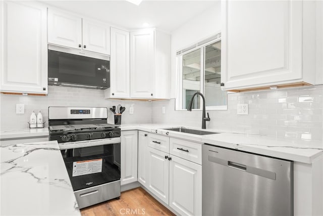 kitchen with appliances with stainless steel finishes, a sink, white cabinetry, and light stone countertops