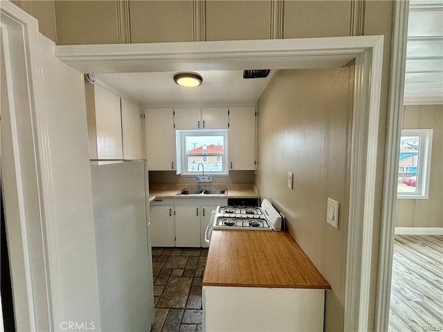 kitchen with white appliances, stone finish flooring, white cabinets, and a sink