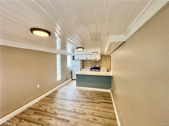 kitchen featuring light wood finished floors, baseboards, freestanding refrigerator, light countertops, and stainless steel stove