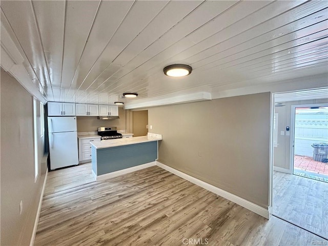 kitchen with light wood-style flooring, freestanding refrigerator, stainless steel range with gas stovetop, and a peninsula