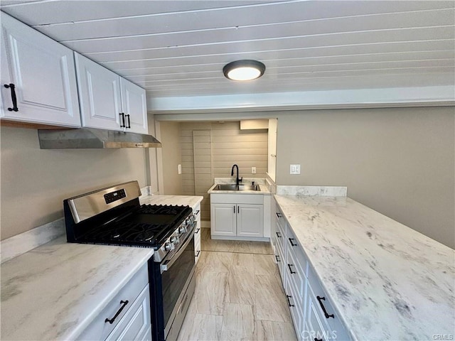 kitchen with white cabinetry, a sink, light stone countertops, under cabinet range hood, and gas range