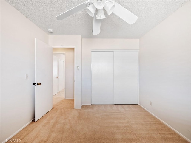 unfurnished bedroom featuring a ceiling fan, a closet, light colored carpet, and a textured ceiling