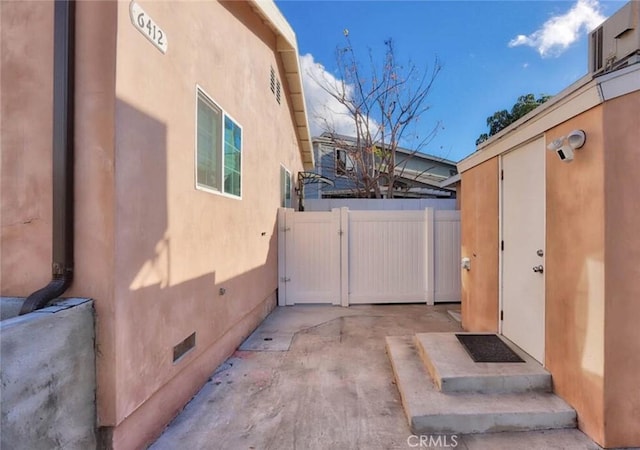 view of side of home with crawl space, fence, a gate, and stucco siding