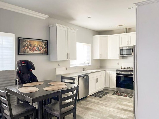 kitchen featuring stainless steel appliances, a sink, white cabinets, light countertops, and light wood finished floors