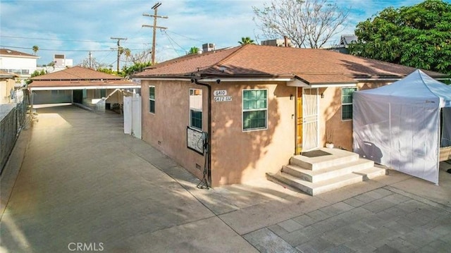 exterior space featuring roof with shingles, fence, and stucco siding