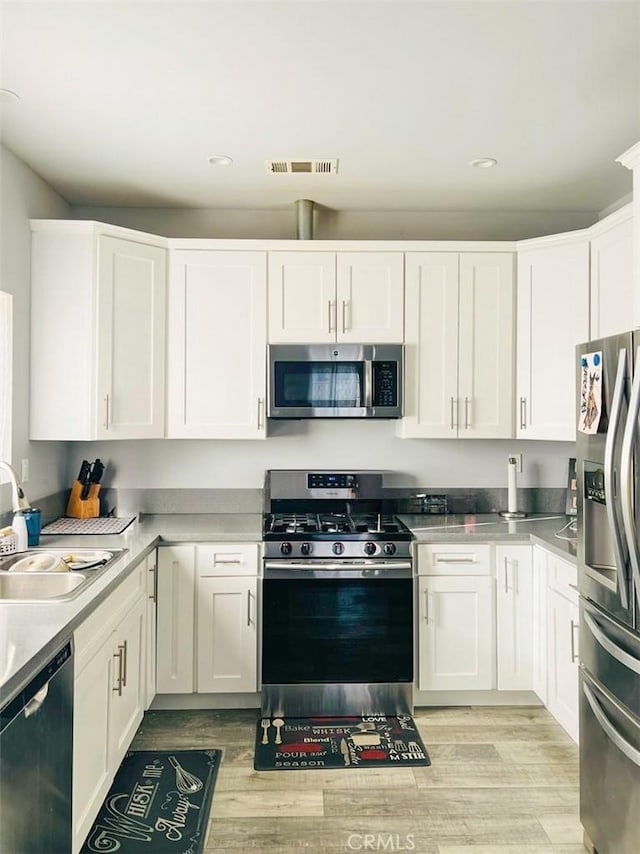 kitchen with stainless steel appliances, a sink, visible vents, and white cabinets