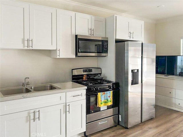 kitchen with stainless steel appliances, a sink, light wood-style floors, white cabinets, and ornamental molding