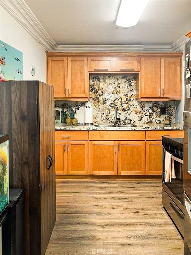 kitchen featuring light stone countertops, a sink, light wood-style floors, decorative backsplash, and crown molding