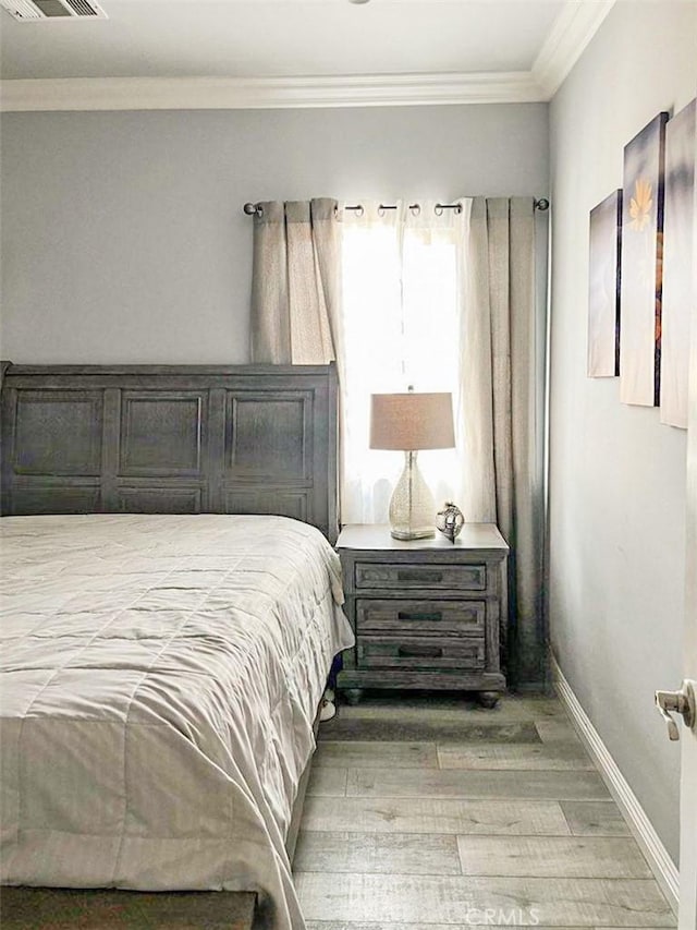 bedroom featuring visible vents, baseboards, crown molding, and wood finished floors