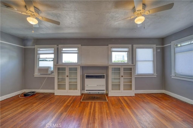 unfurnished living room featuring heating unit, a wealth of natural light, and wood finished floors