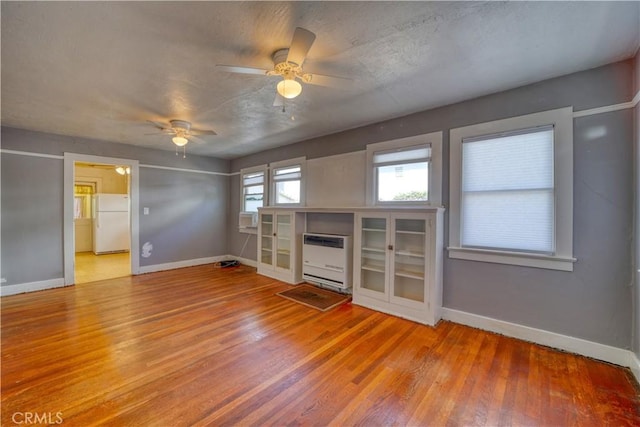 unfurnished living room featuring baseboards, ceiling fan, wood finished floors, and heating unit