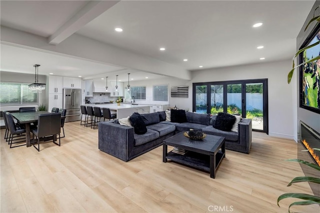 living room featuring light wood-style flooring, a fireplace with flush hearth, beamed ceiling, and recessed lighting