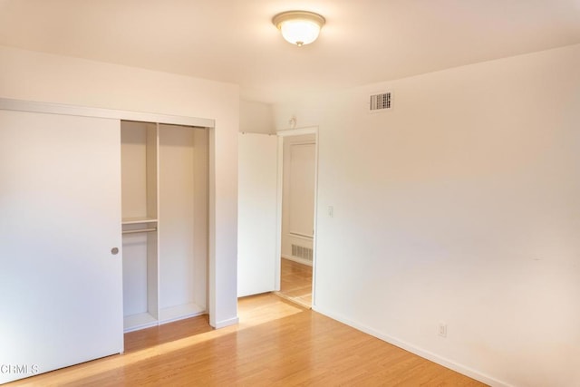 unfurnished bedroom with a closet, visible vents, baseboards, and wood finished floors