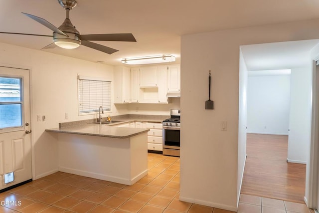 kitchen featuring white cabinets, a sink, a peninsula, under cabinet range hood, and stainless steel gas range oven