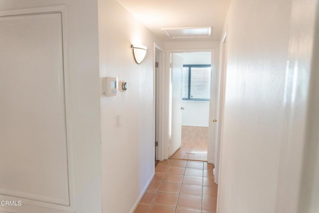 corridor featuring light tile patterned flooring and attic access