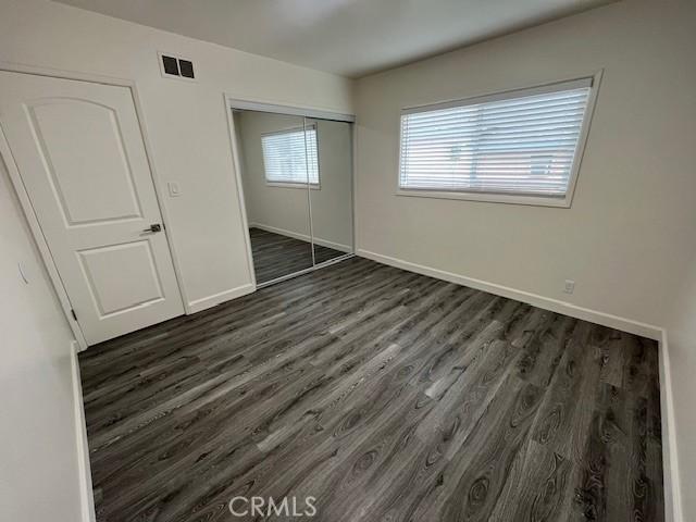 unfurnished bedroom featuring a closet, dark wood-style flooring, visible vents, and baseboards