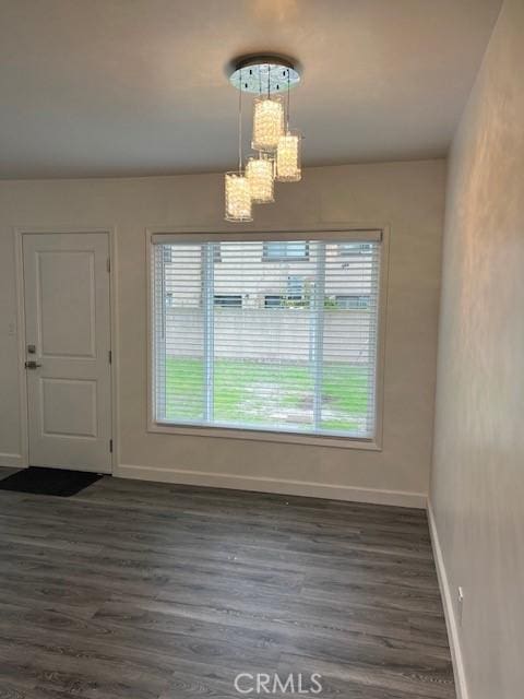 unfurnished dining area with baseboards, dark wood finished floors, and a notable chandelier