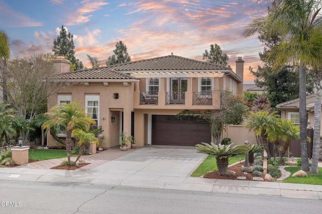 mediterranean / spanish-style house with a tile roof, stucco siding, concrete driveway, a balcony, and a garage