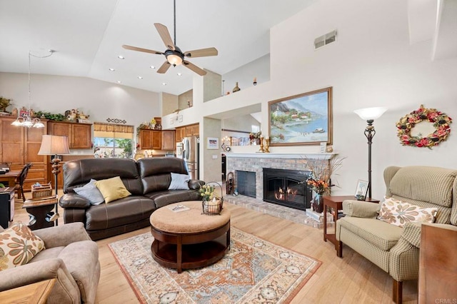 living room featuring visible vents, light wood-style floors, a glass covered fireplace, a ceiling fan, and high vaulted ceiling