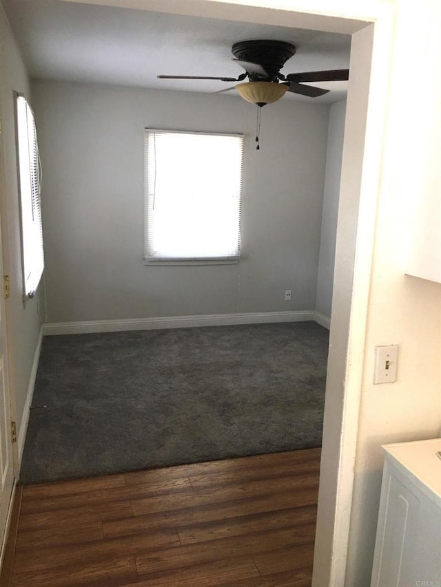 spare room with dark wood-style floors, dark colored carpet, a ceiling fan, and baseboards