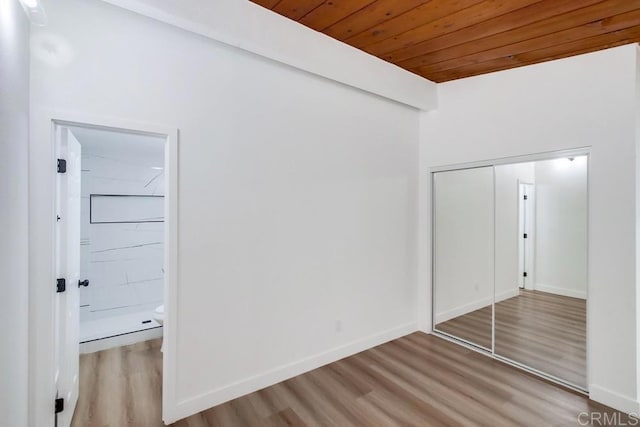 unfurnished bedroom with a closet, wooden ceiling, wood finished floors, and baseboards