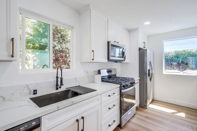 kitchen with stainless steel appliances, light wood-style flooring, white cabinets, a sink, and light stone countertops