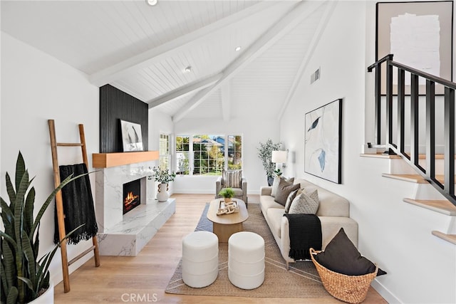 living area featuring beam ceiling, visible vents, stairway, a high end fireplace, and wood finished floors