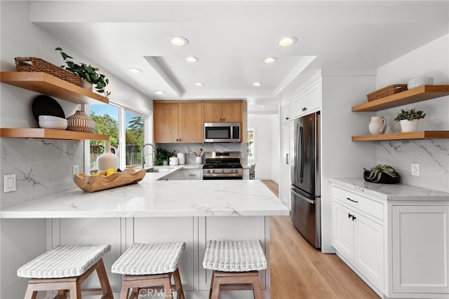 kitchen featuring appliances with stainless steel finishes, a peninsula, a tray ceiling, open shelves, and a sink