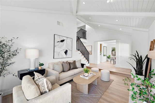 living area featuring light wood-style flooring, visible vents, baseboards, stairs, and beam ceiling