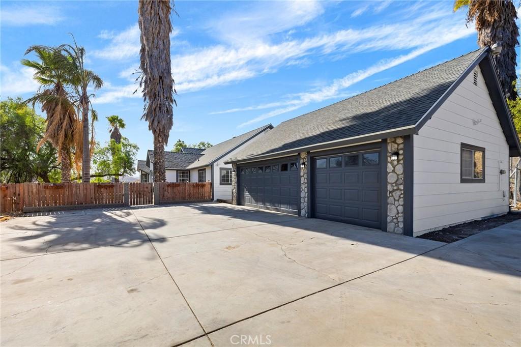 view of property exterior featuring a garage, a shingled roof, fence, stone siding, and driveway