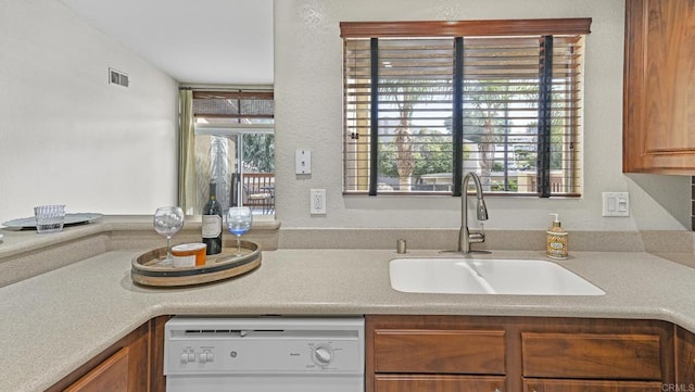 kitchen with white dishwasher, a sink, visible vents, light countertops, and brown cabinets