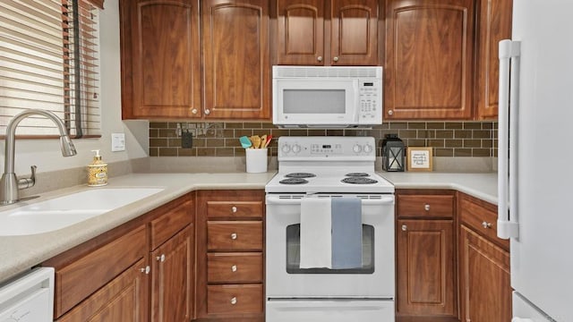 kitchen featuring white appliances, backsplash, light countertops, and a sink