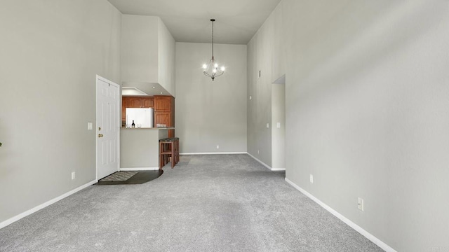 carpeted empty room with a chandelier, a towering ceiling, and baseboards