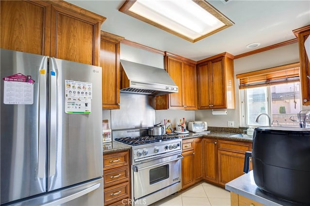 kitchen with light tile patterned floors, stainless steel appliances, a sink, wall chimney range hood, and brown cabinets