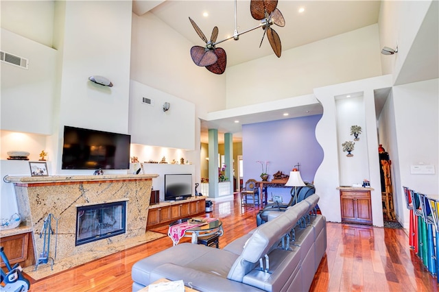 living area with a high ceiling, visible vents, a fireplace, and hardwood / wood-style floors