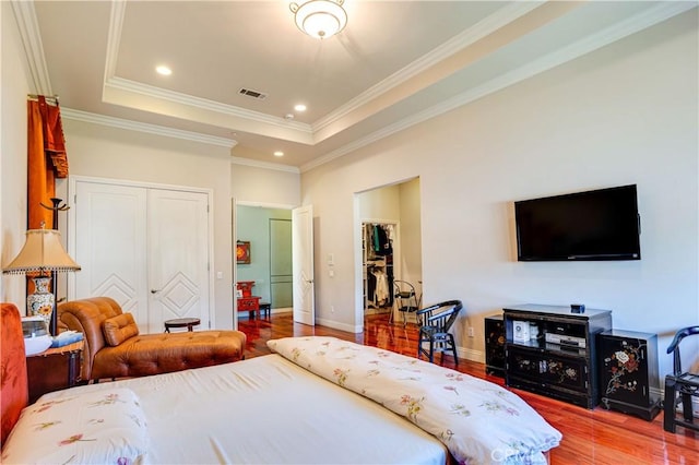 bedroom featuring baseboards, visible vents, wood finished floors, a tray ceiling, and crown molding