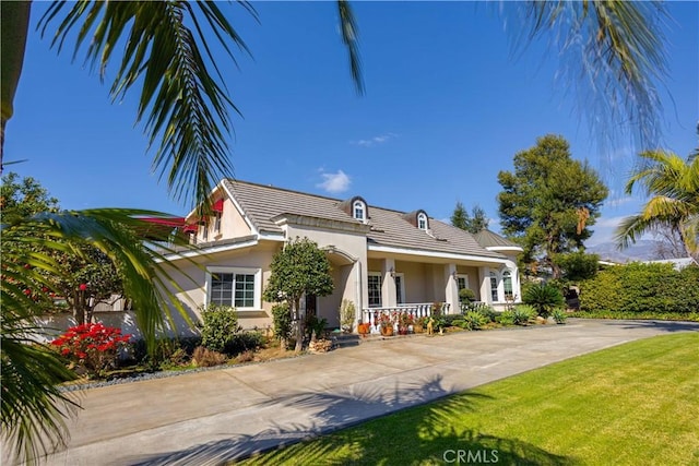 view of front facade featuring a porch, a tile roof, concrete driveway, stucco siding, and a front lawn