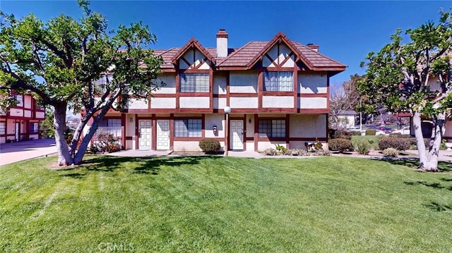 tudor house featuring a front lawn, a chimney, and stucco siding