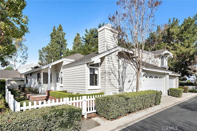 view of front of property with a fenced front yard, driveway, a chimney, and a garage