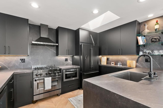 kitchen featuring a skylight, premium appliances, wall chimney exhaust hood, a sink, and recessed lighting