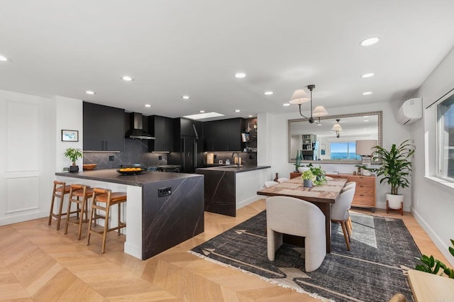 kitchen with tasteful backsplash, dark countertops, recessed lighting, a wall mounted AC, and wall chimney range hood