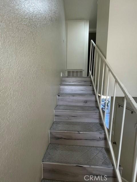 stairway with visible vents, wood finished floors, and a textured wall