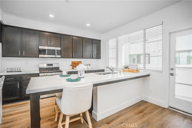 kitchen with light wood-style flooring, stainless steel appliances, a sink, light countertops, and a kitchen bar