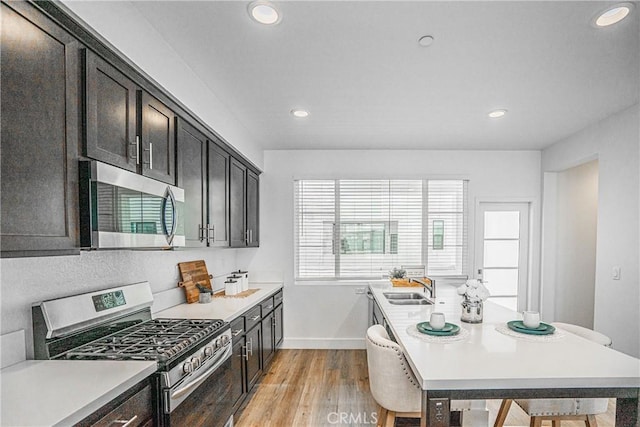 kitchen with a sink, baseboards, light wood-style floors, light countertops, and appliances with stainless steel finishes