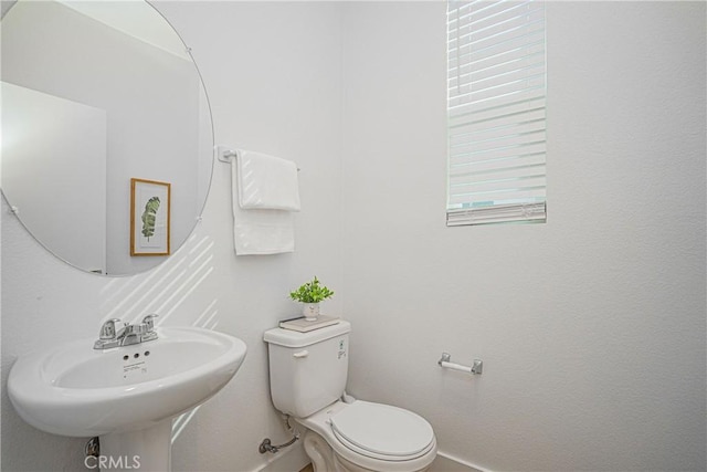 half bathroom with a sink, toilet, and baseboards