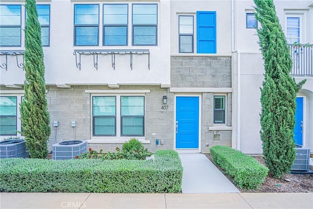 view of exterior entry featuring stone siding, stucco siding, and central AC unit