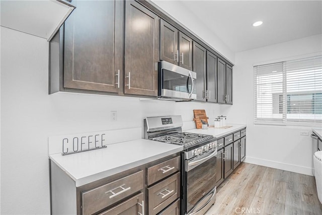 kitchen featuring stainless steel appliances, light countertops, light wood-style floors, dark brown cabinetry, and baseboards