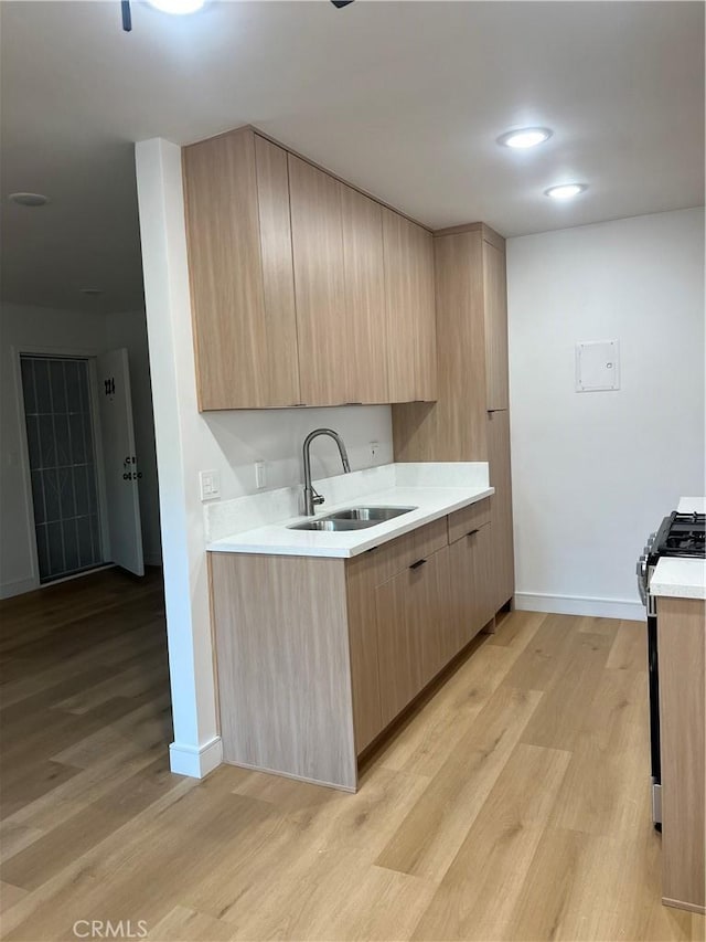 kitchen with a sink, light countertops, stainless steel gas stove, light brown cabinetry, and modern cabinets